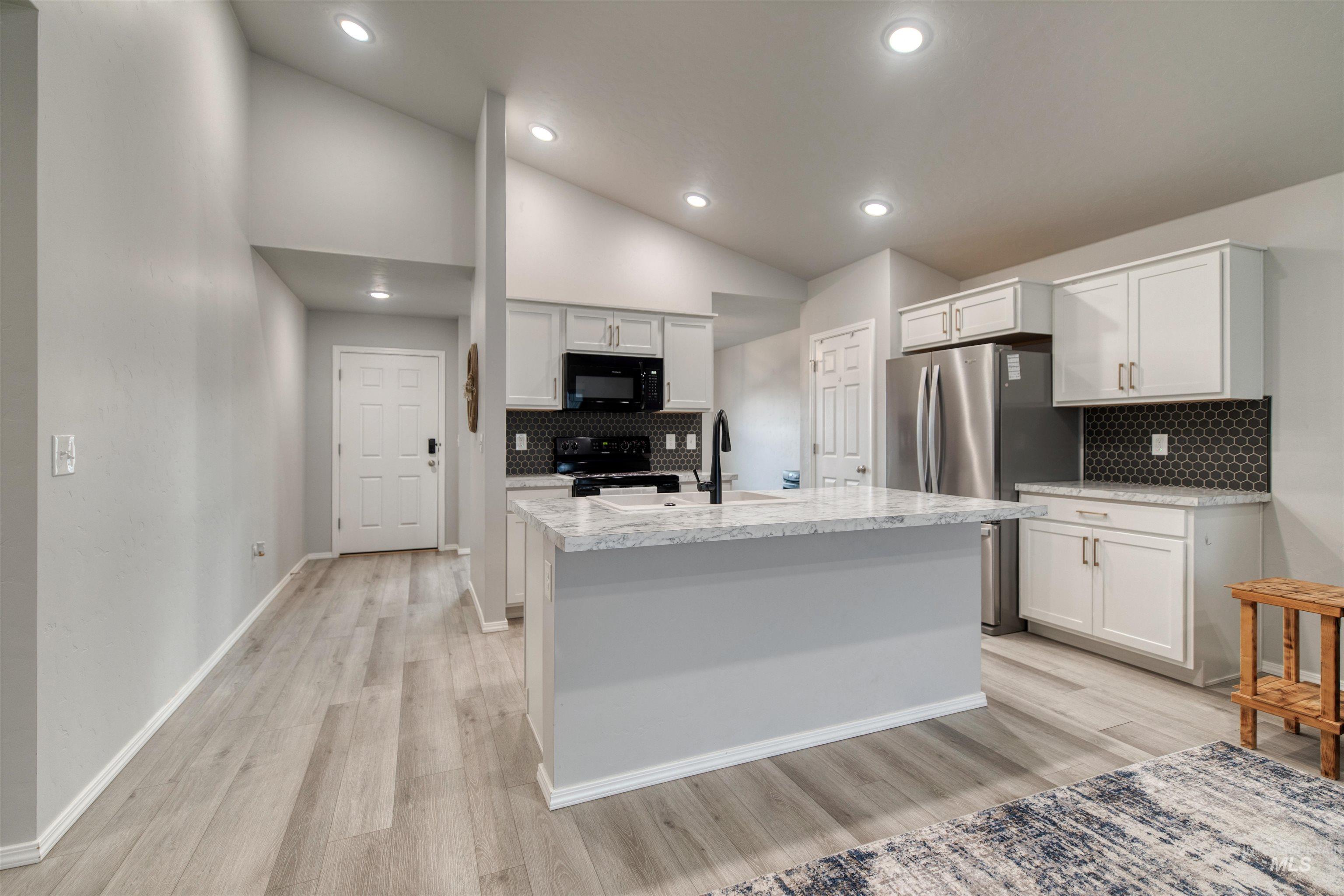 Kitchen with backsplash, black appliances, light wood-style floors, white cabinetry, and light stone countertops