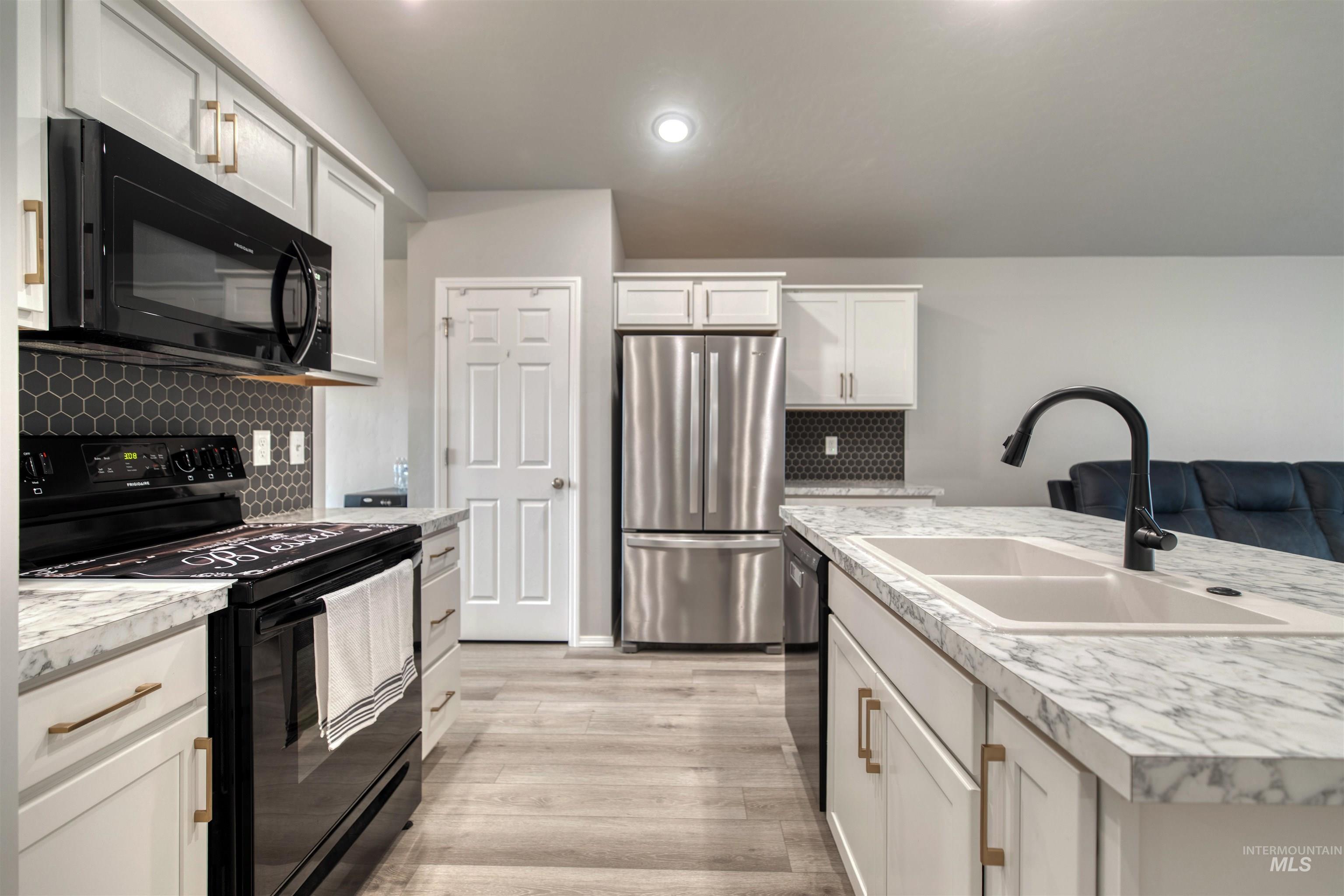 Kitchen featuring black appliances, light countertops, white cabinets, tasteful backsplash, and light wood-type flooring