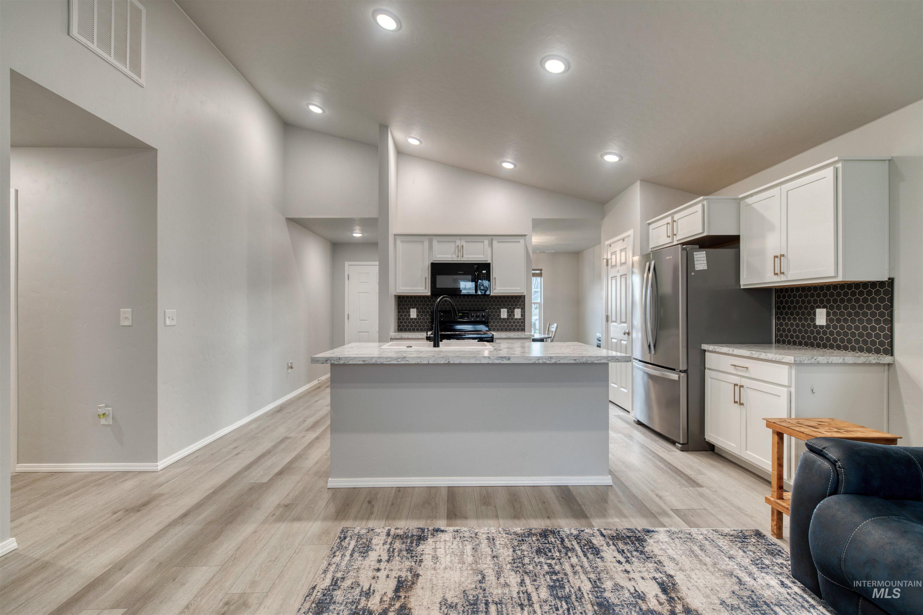 Kitchen featuring white cabinets, decorative backsplash, vaulted ceiling, light wood finished floors, and black appliances