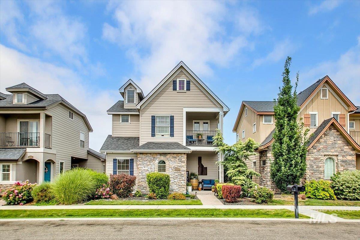 View of front of property featuring stone siding, a balcony, a front yard, and a shingled roof