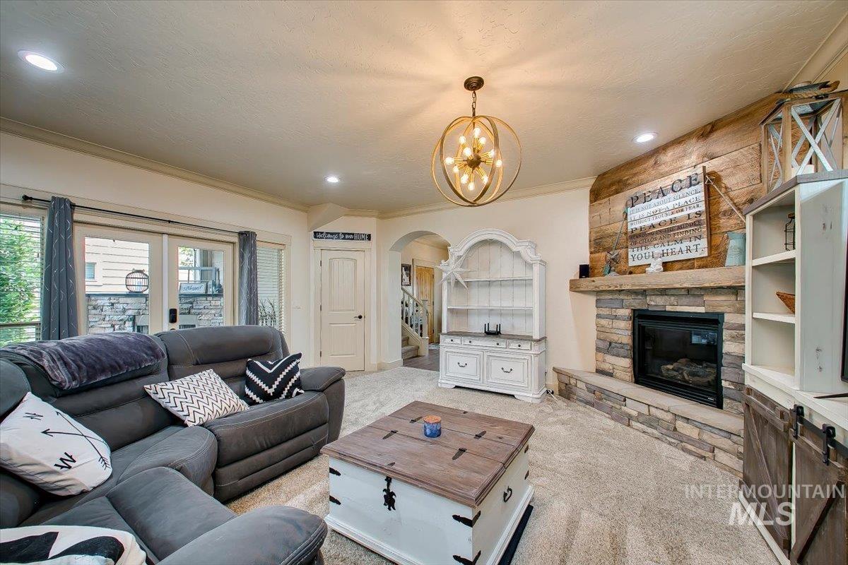 Carpeted living room with a fireplace, arched walkways, crown molding, a chandelier, and a textured ceiling