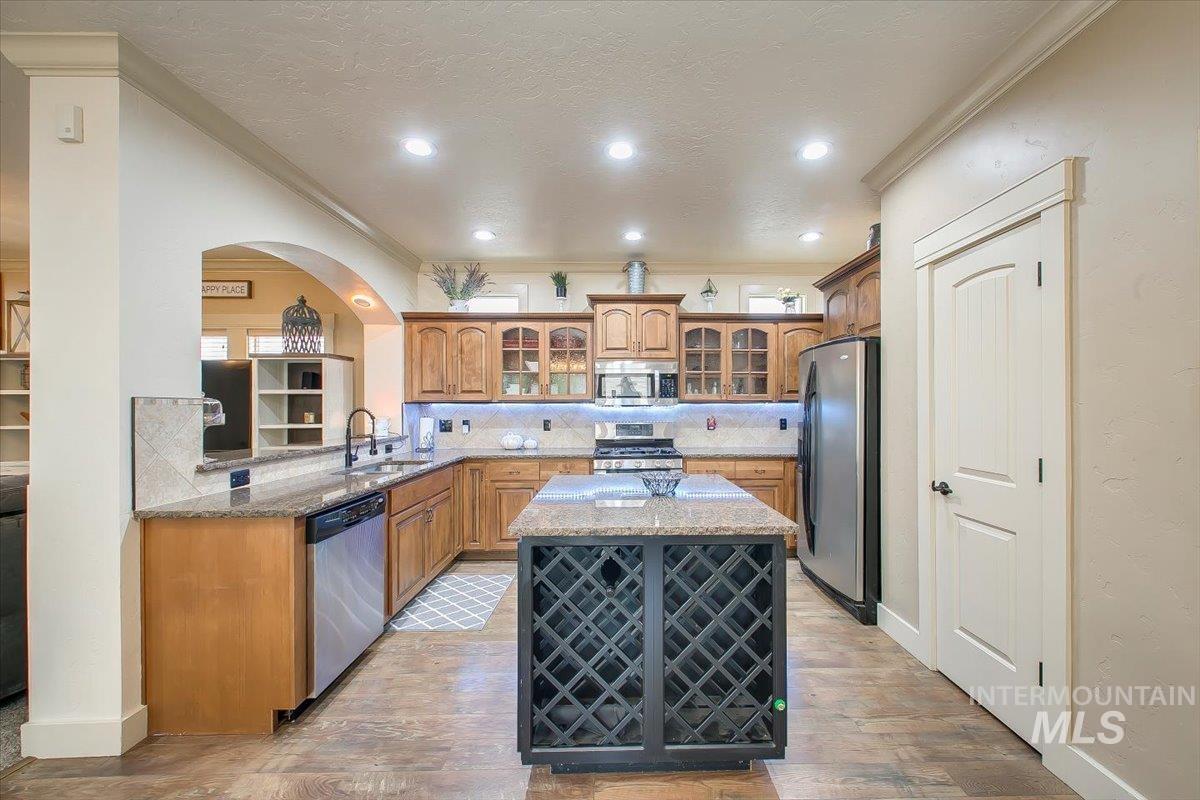 Kitchen with glass insert cabinets, light stone countertops, a center island, tasteful backsplash, and stainless steel appliances
