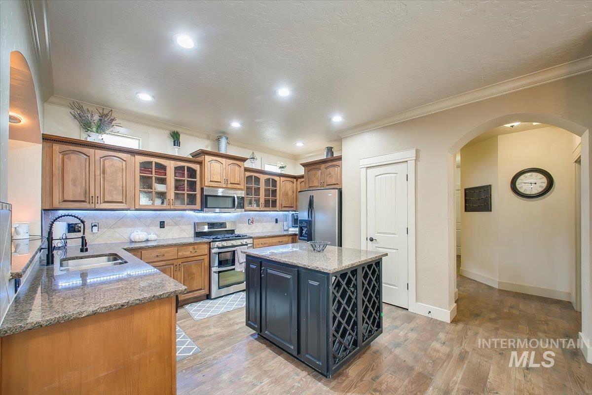 Kitchen featuring glass insert cabinets, arched walkways, light stone counters, appliances with stainless steel finishes, and a kitchen island