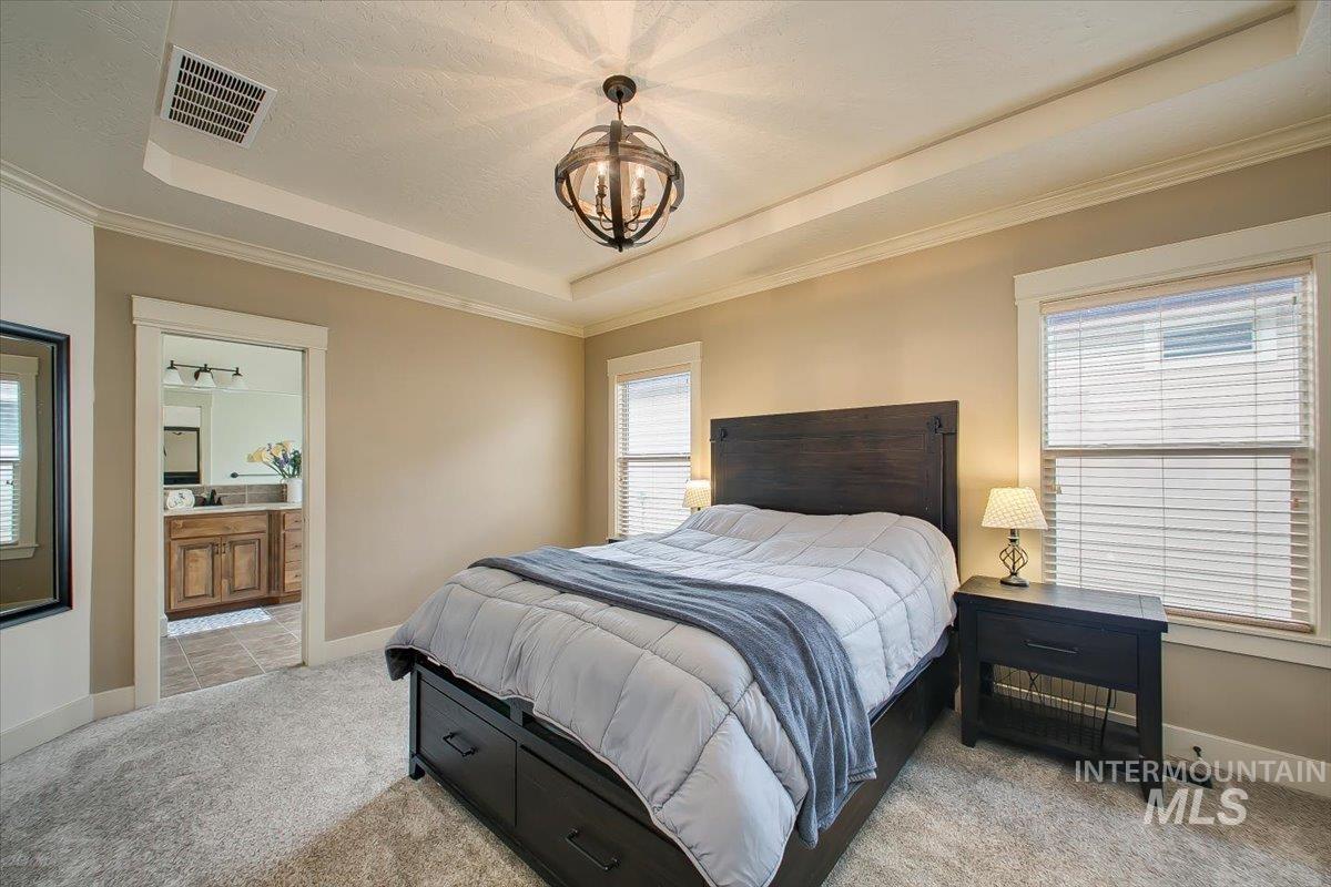 Bedroom with a raised ceiling, a chandelier, light carpet, and ornamental molding