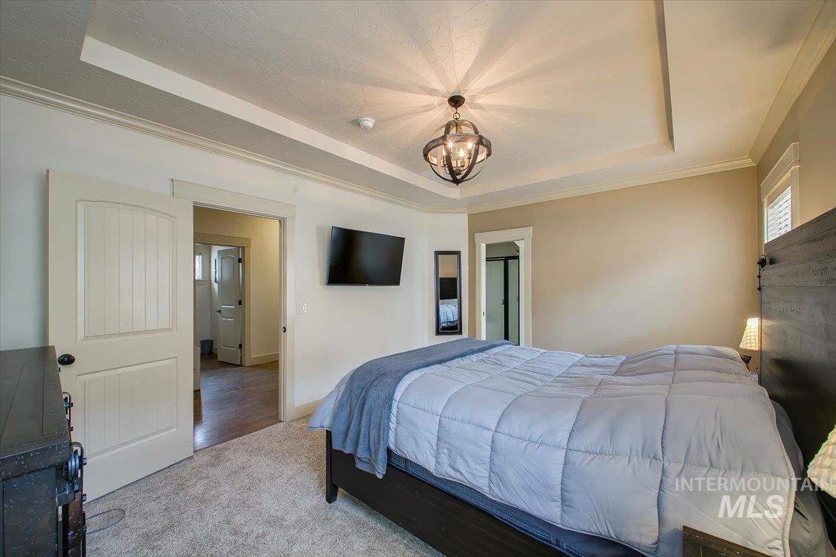Bedroom featuring a tray ceiling, carpet floors, a chandelier, and crown molding
