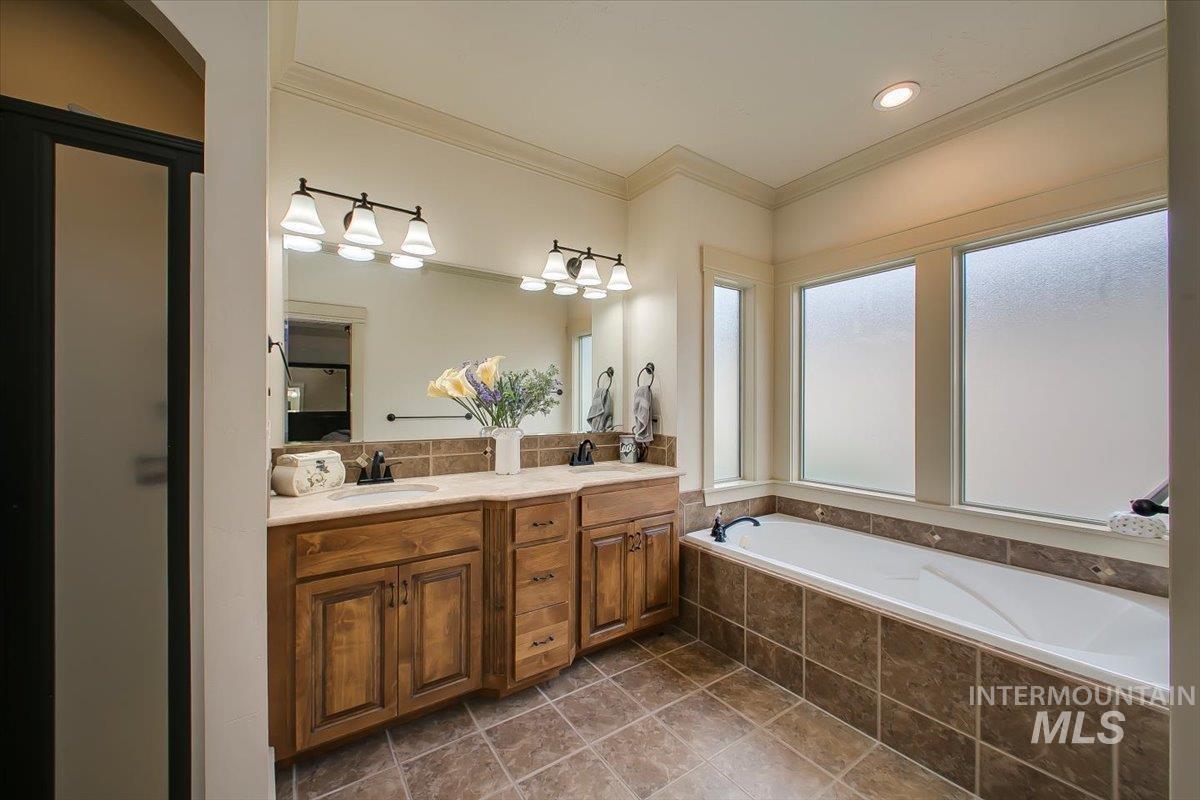Full bathroom featuring ornamental molding, double vanity, and a garden tub