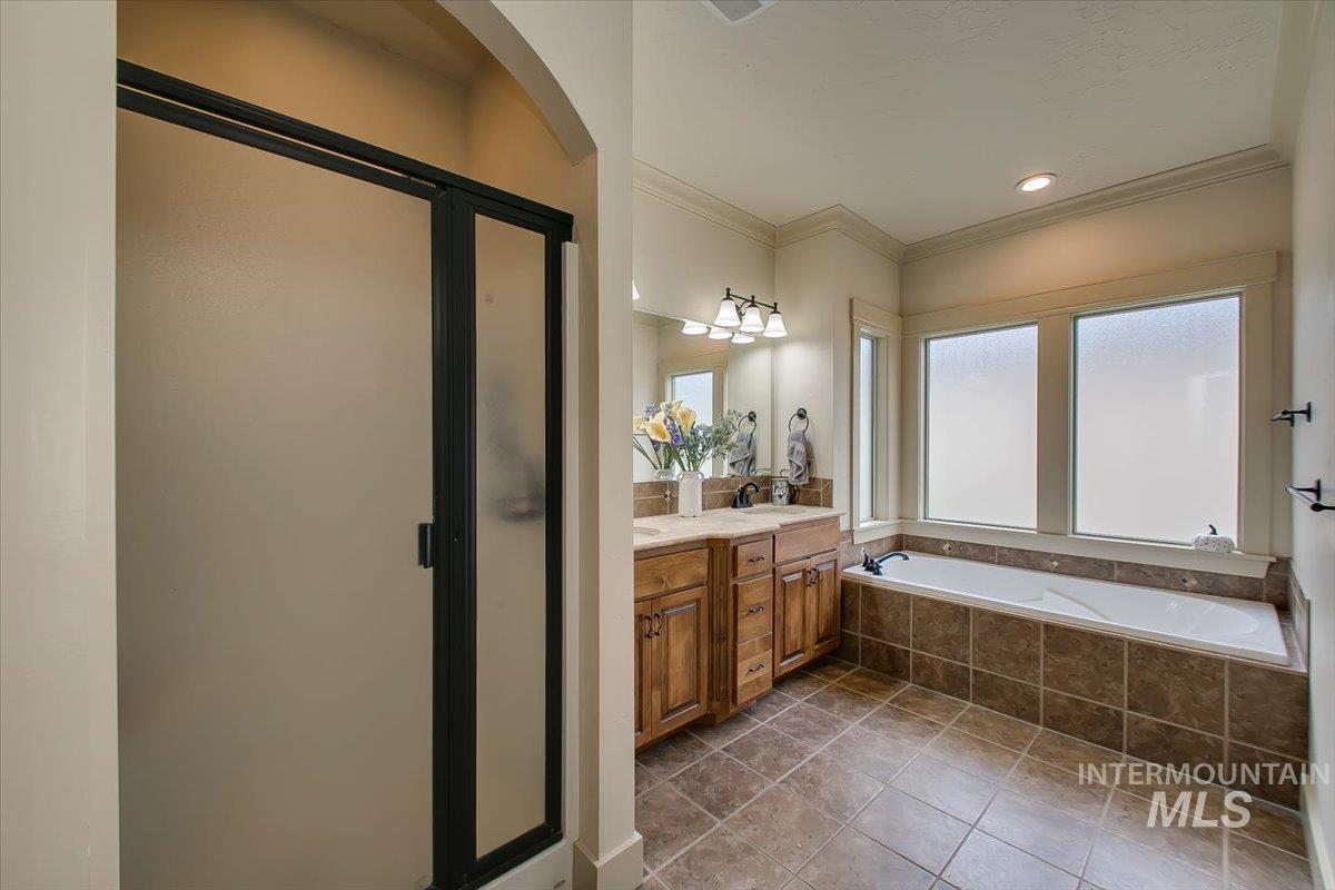 Full bath featuring crown molding, double vanity, a shower stall, a garden tub, and dark tile patterned flooring