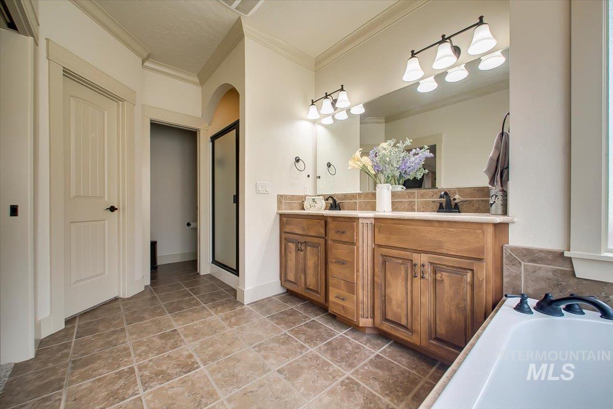 Bathroom featuring double vanity, a garden tub, ornamental molding, and a stall shower