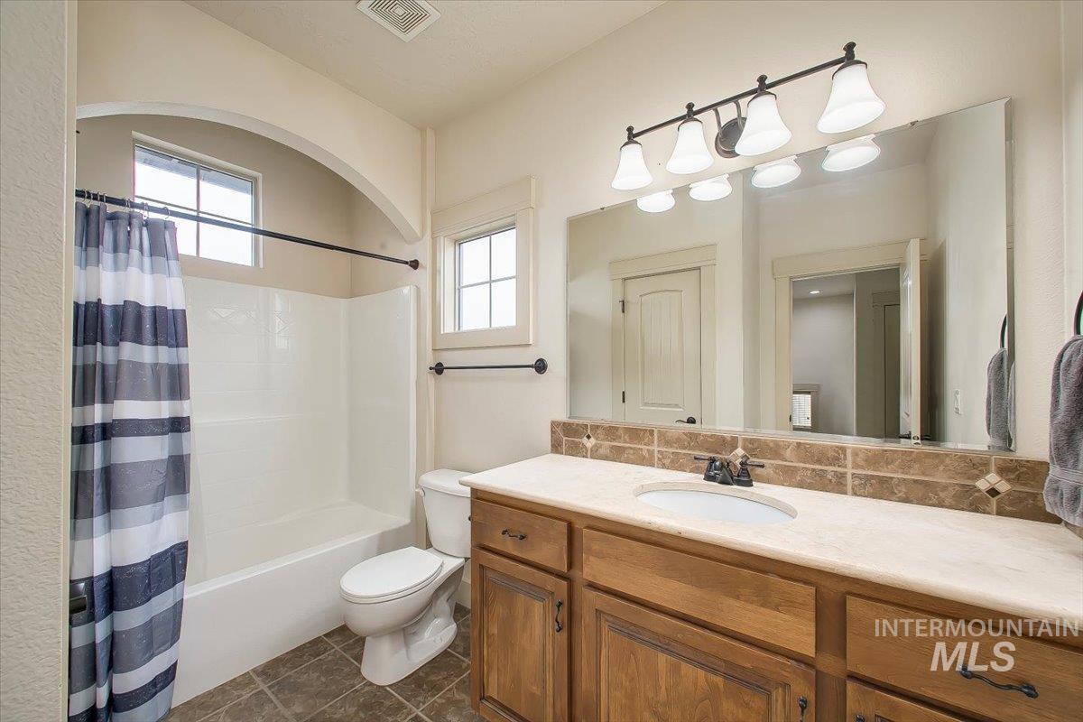 Bathroom featuring vanity, shower / bath combo, decorative backsplash, and dark tile patterned floors