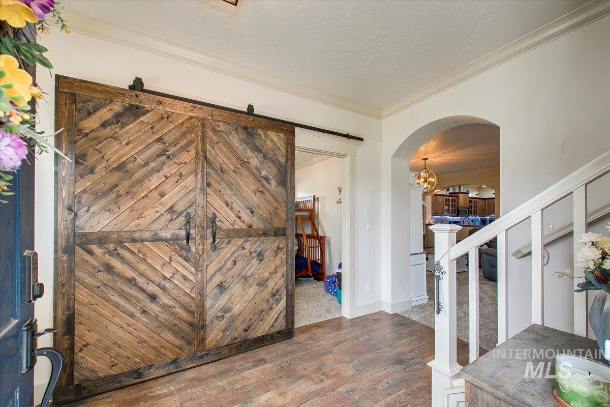 Foyer entrance featuring arched walkways, stairs, a barn door, ornamental molding, and wood finished floors