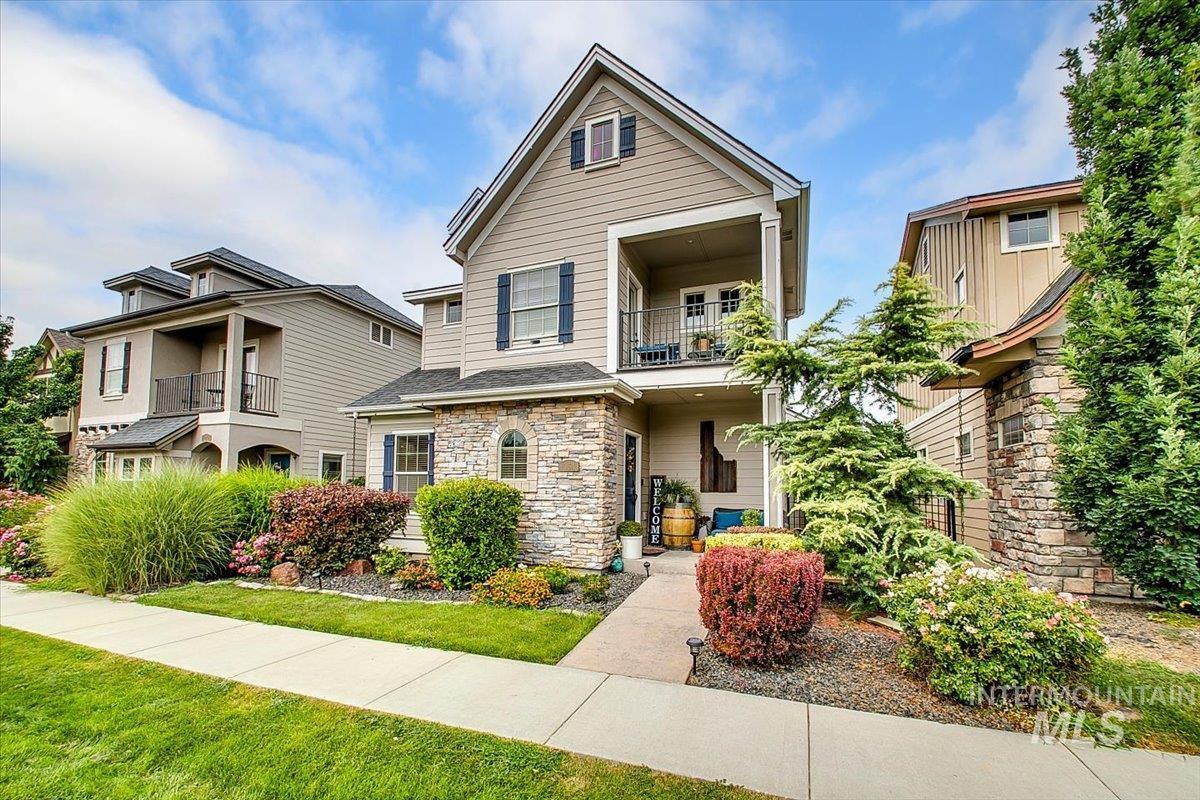 View of front of house with a balcony, stone siding, and a front lawn