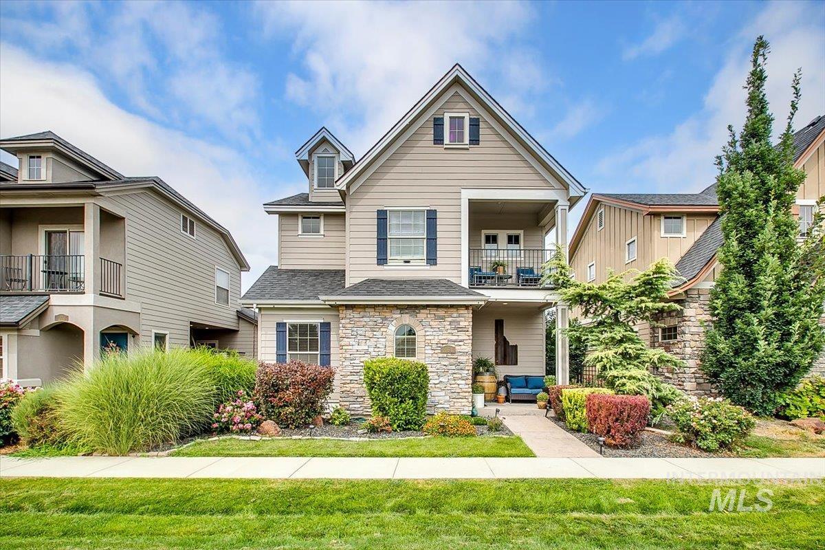 Traditional-style house featuring stone siding, a balcony, roof with shingles, and a front yard