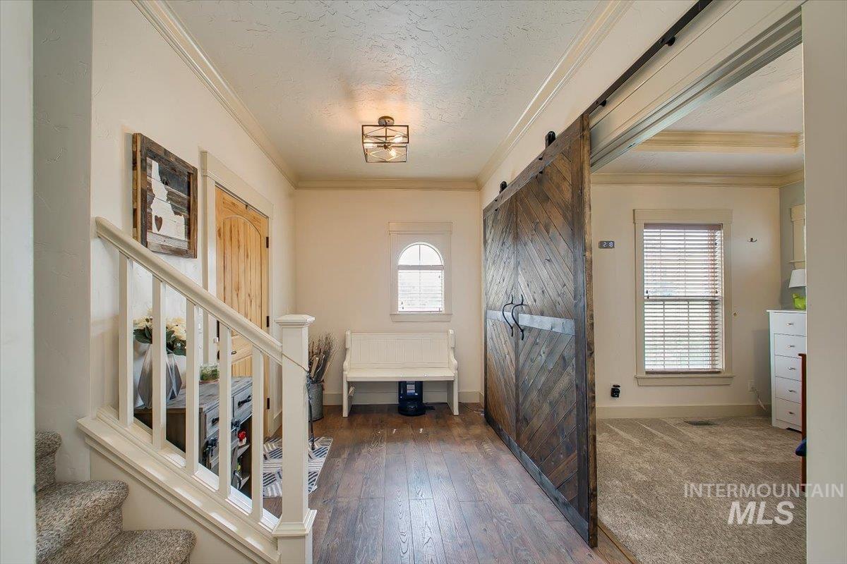 Entrance foyer with ornamental molding, stairway, hardwood / wood-style flooring, a barn door, and a textured ceiling