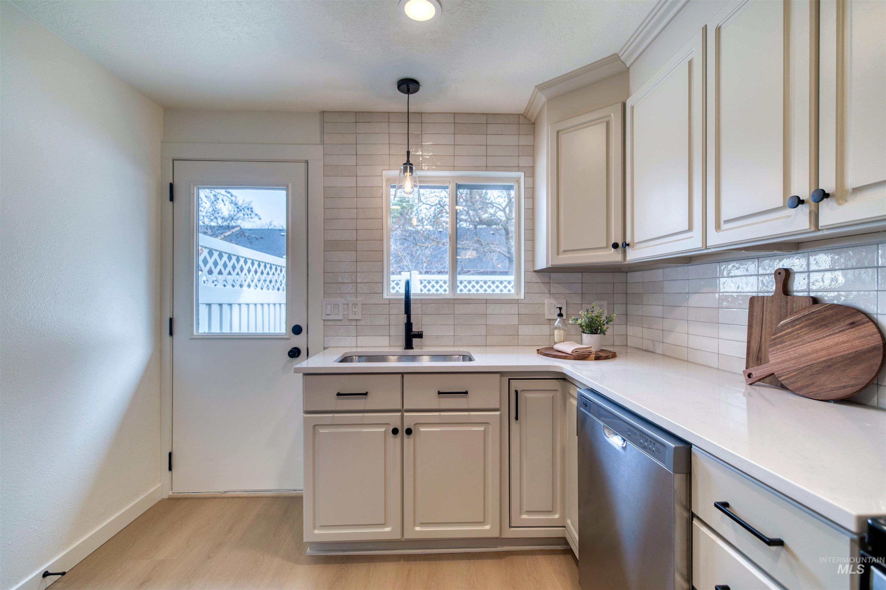 Kitchen featuring decorative backsplash, stainless steel dishwasher, hanging light fixtures, light wood finished floors, and a textured ceiling
