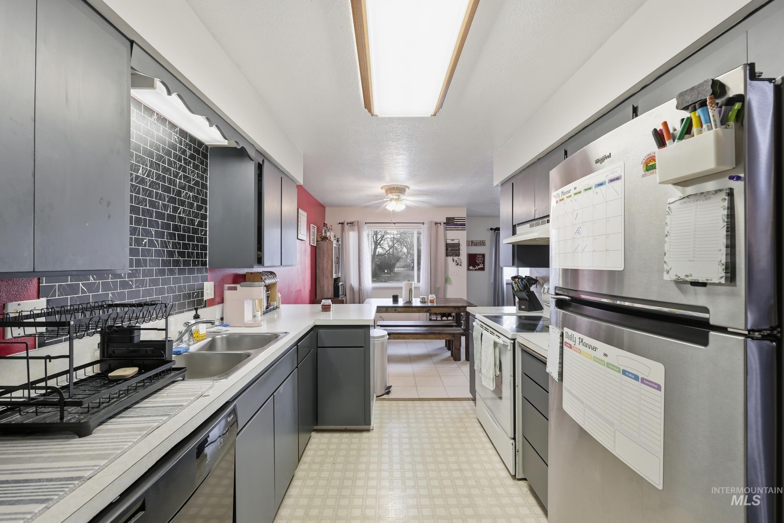 Kitchen featuring freestanding refrigerator, light flooring, electric stove, gray cabinets, and light countertops