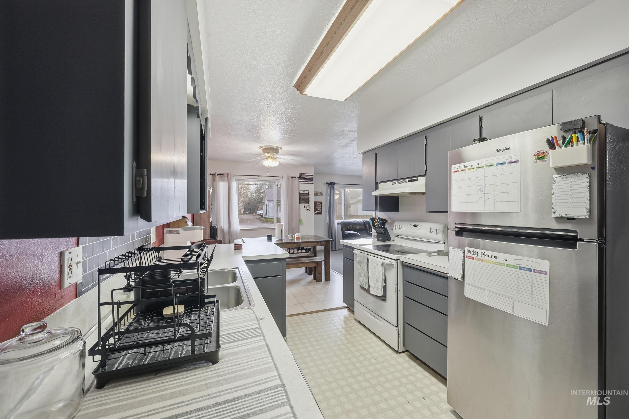 Kitchen featuring freestanding refrigerator, white range with electric stovetop, light countertops, and gray cabinets