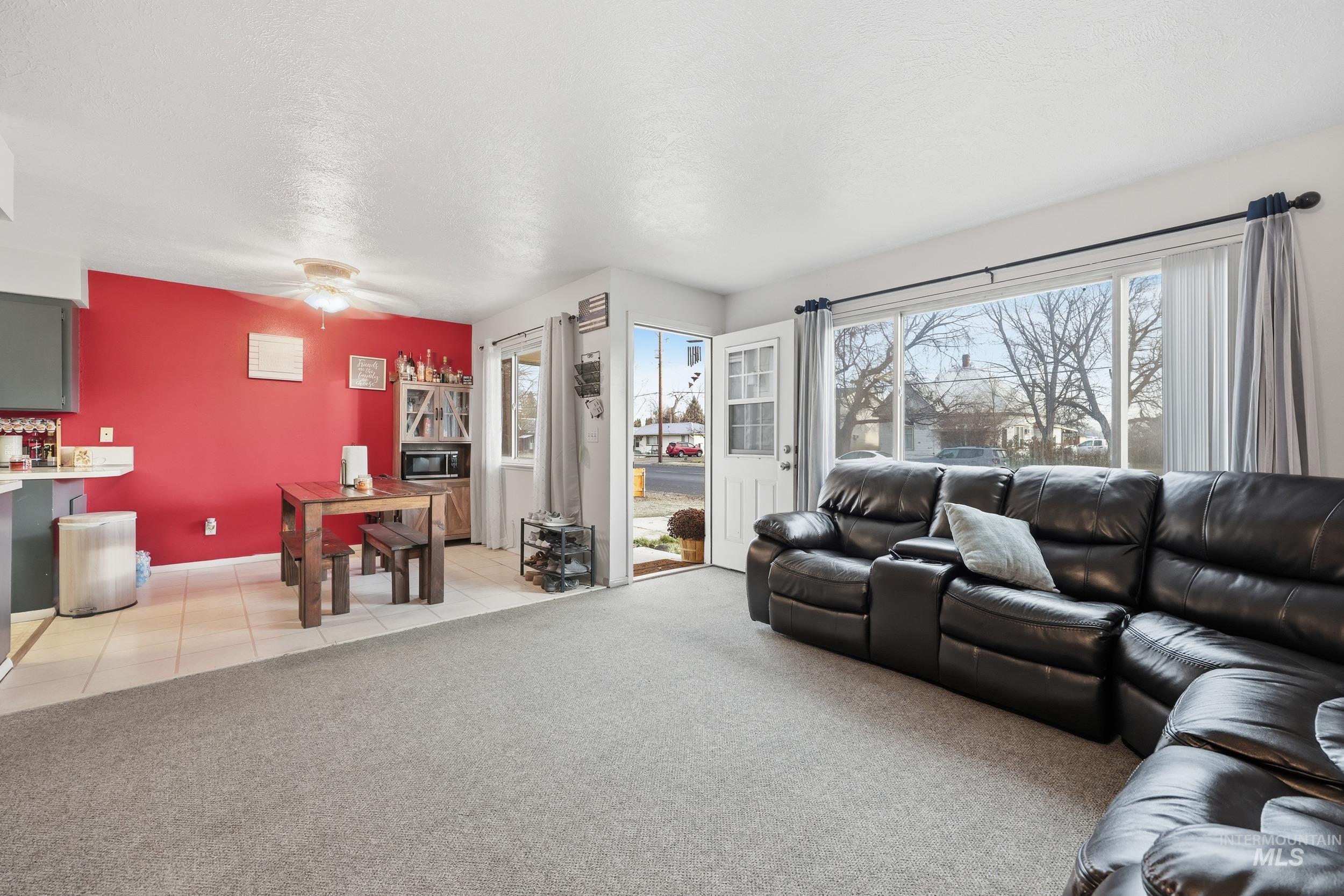 Living room with light colored carpet, a textured ceiling, light tile patterned flooring, and a ceiling fan