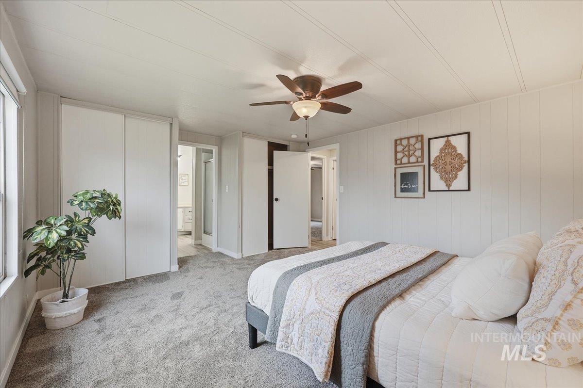 Carpeted bedroom with a closet, a ceiling fan, and wood walls