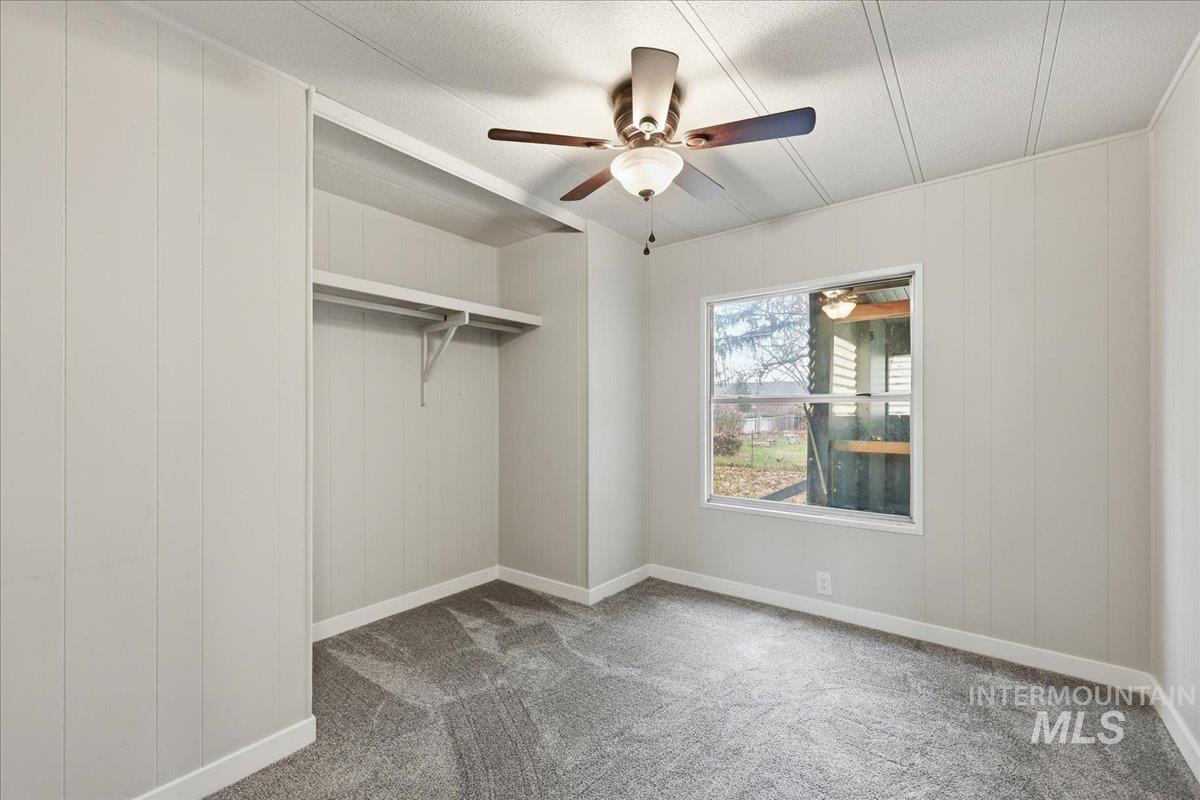 Unfurnished bedroom featuring carpet flooring, wood walls, and ceiling fan