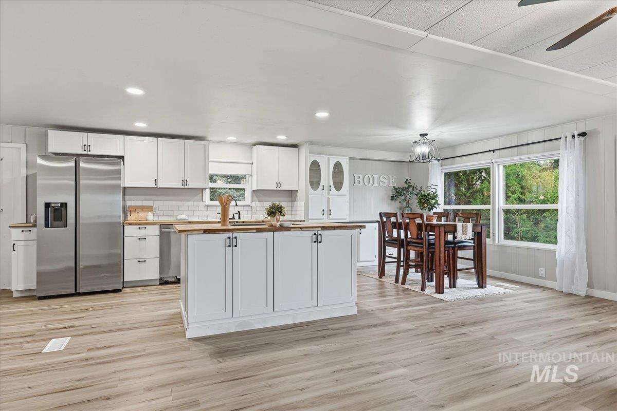 Kitchen with stainless steel fridge with ice dispenser, white cabinets, light wood-style floors, butcher block counters, and recessed lighting