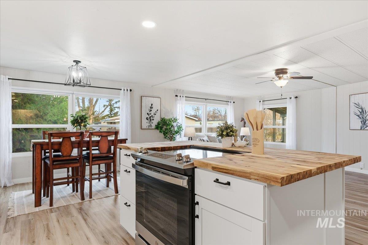 Kitchen with butcher block countertops, stainless steel electric range oven, light wood-style floors, white cabinets, and a center island