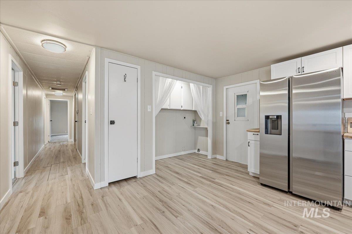 Kitchen with stainless steel refrigerator with ice dispenser, white cabinetry, and light wood finished floors