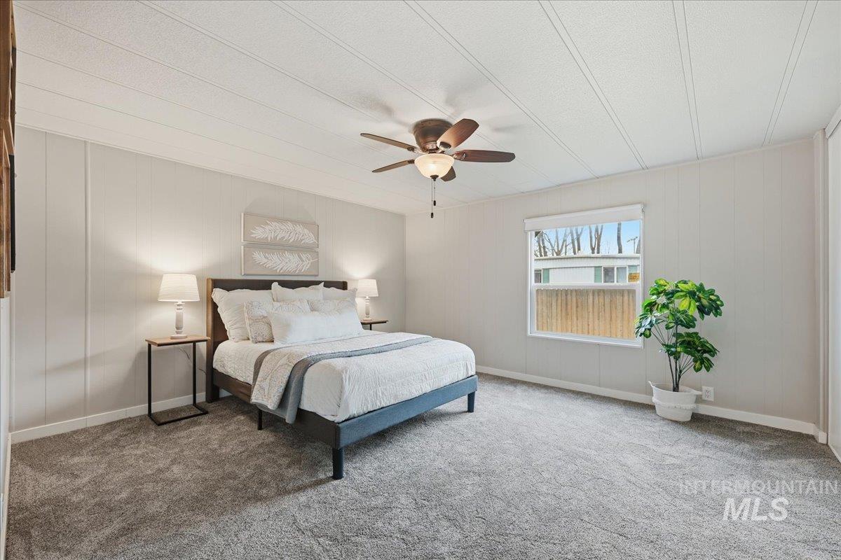 Carpeted bedroom featuring a ceiling fan, wooden walls, and a textured ceiling