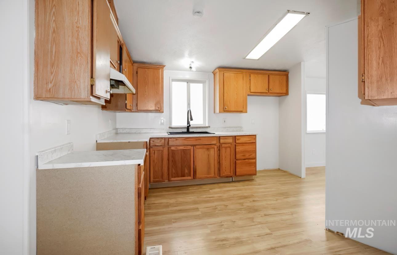 Kitchen featuring light countertops, light wood finished floors, brown cabinets, and under cabinet range hood