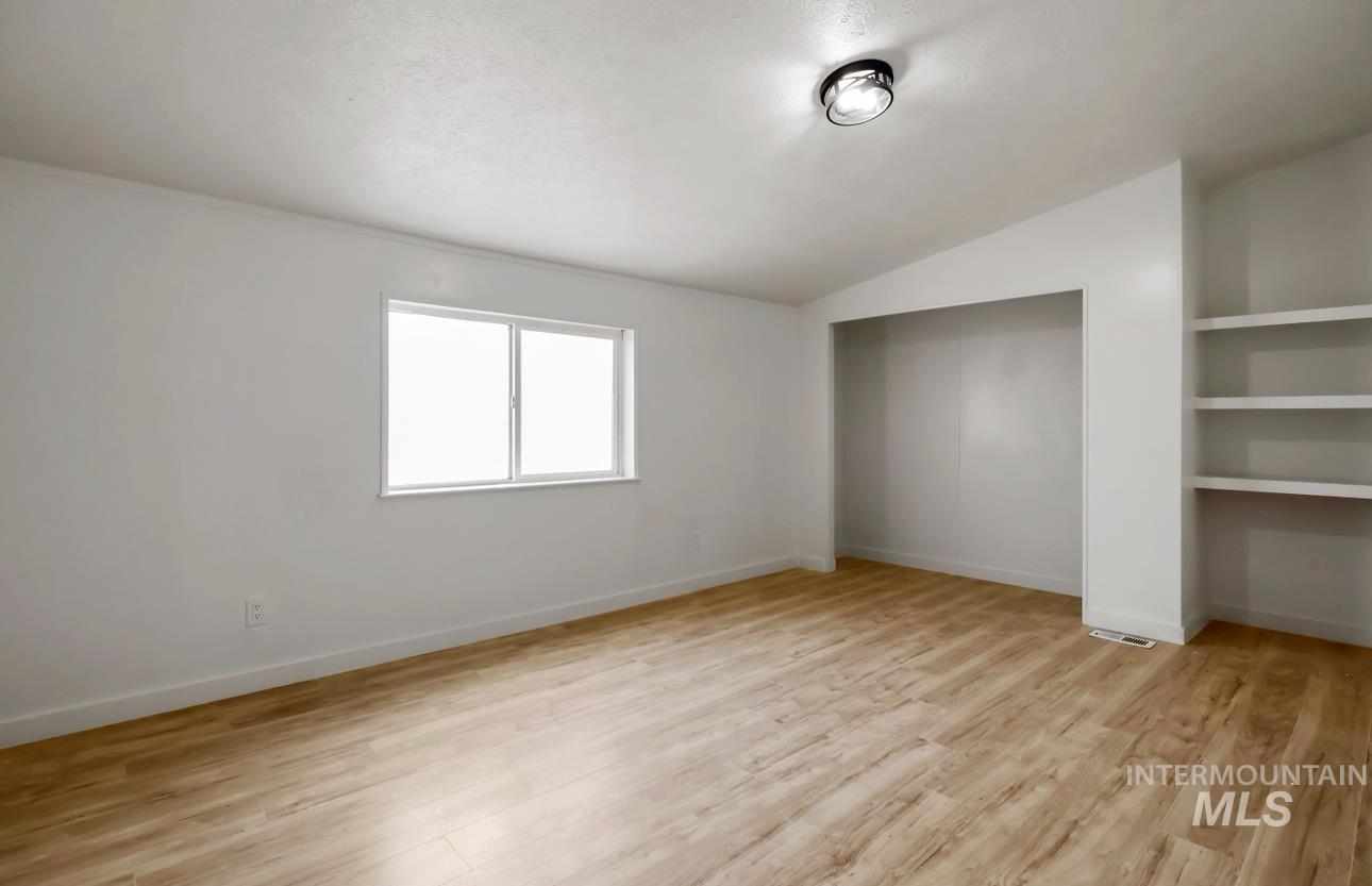 Empty room with light wood-type flooring and lofted ceiling