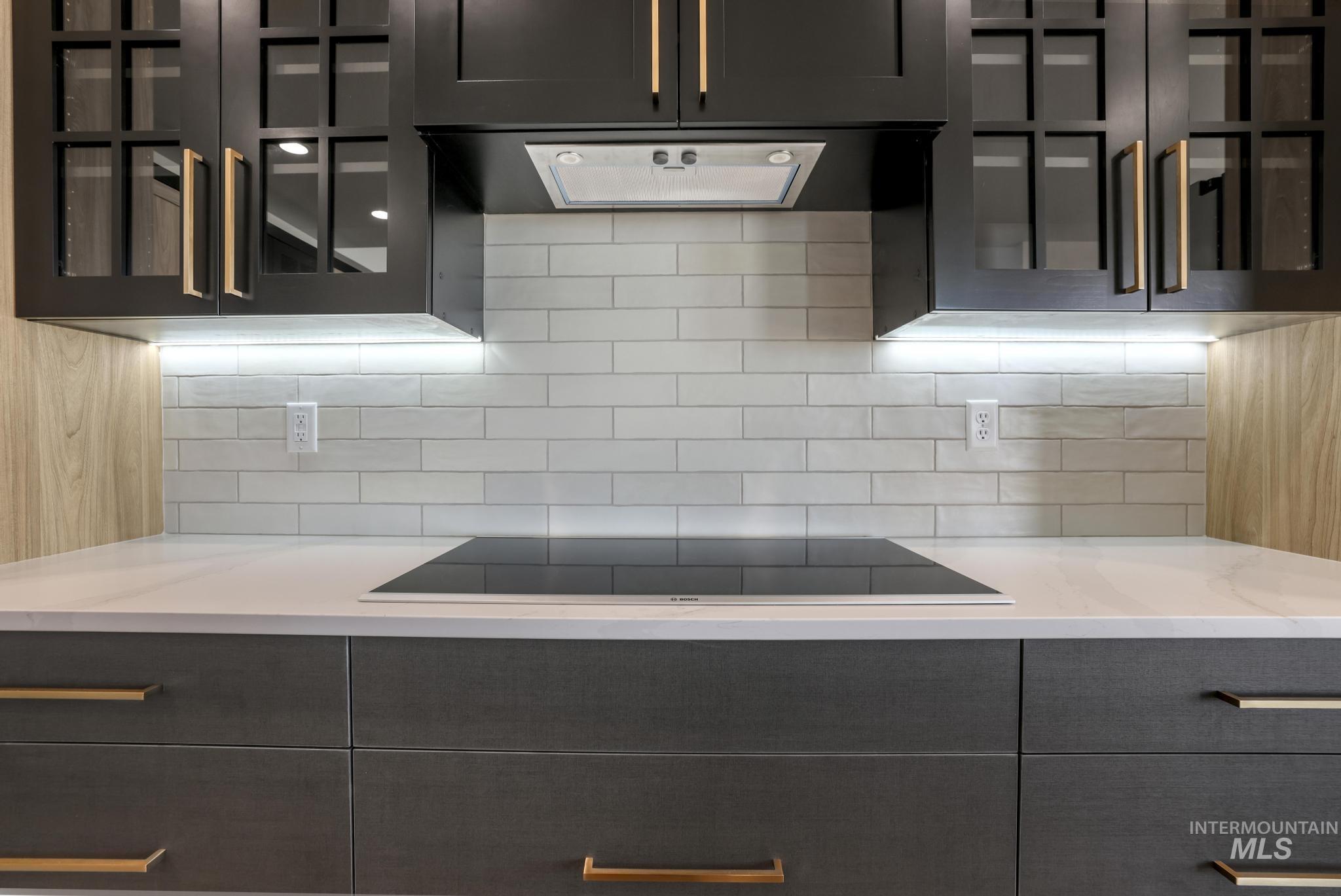 Kitchen featuring glass insert cabinets, tasteful backsplash, black electric stovetop, and light stone countertops
