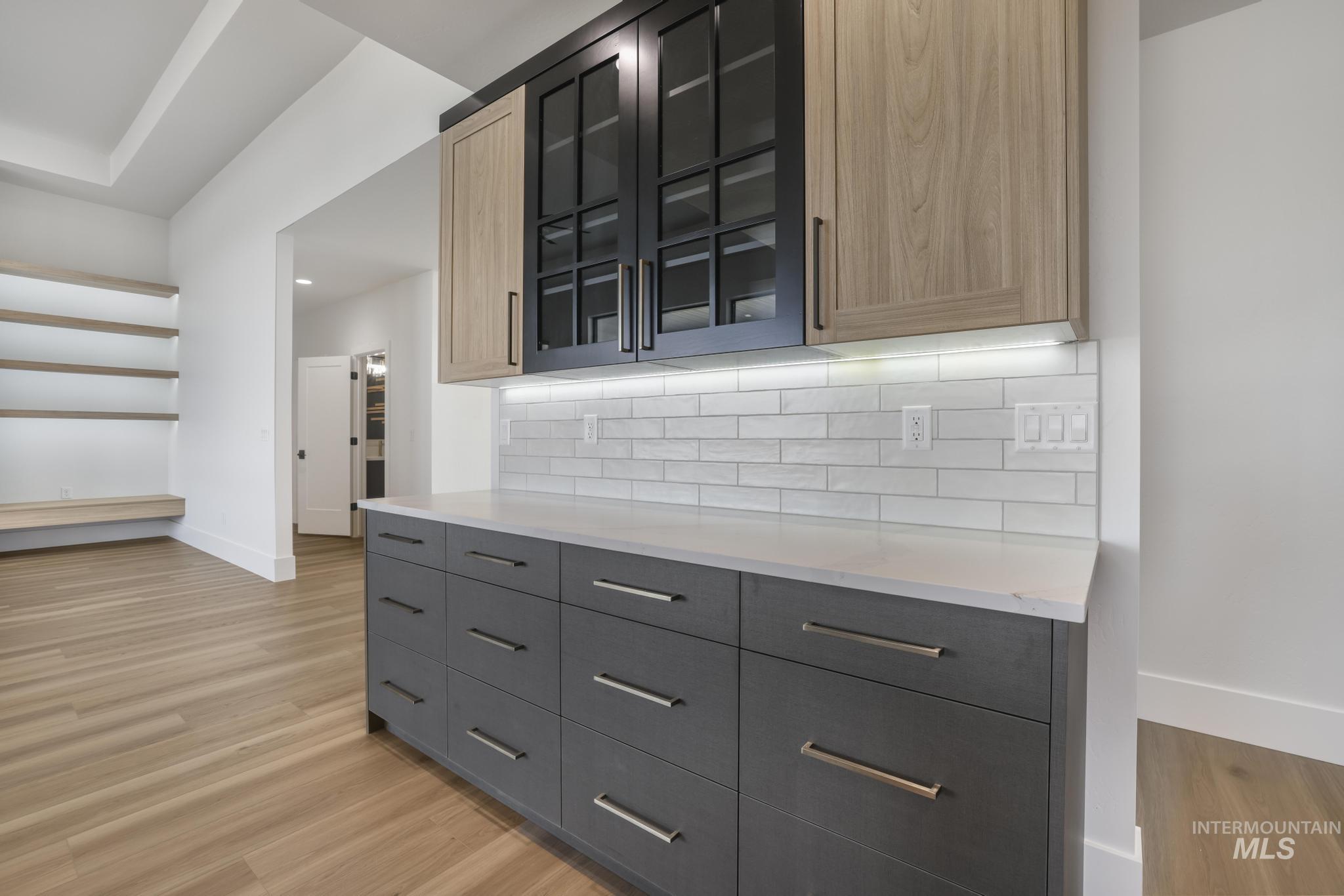 Bar featuring light stone counters, light wood-style flooring, backsplash, and glass insert cabinets