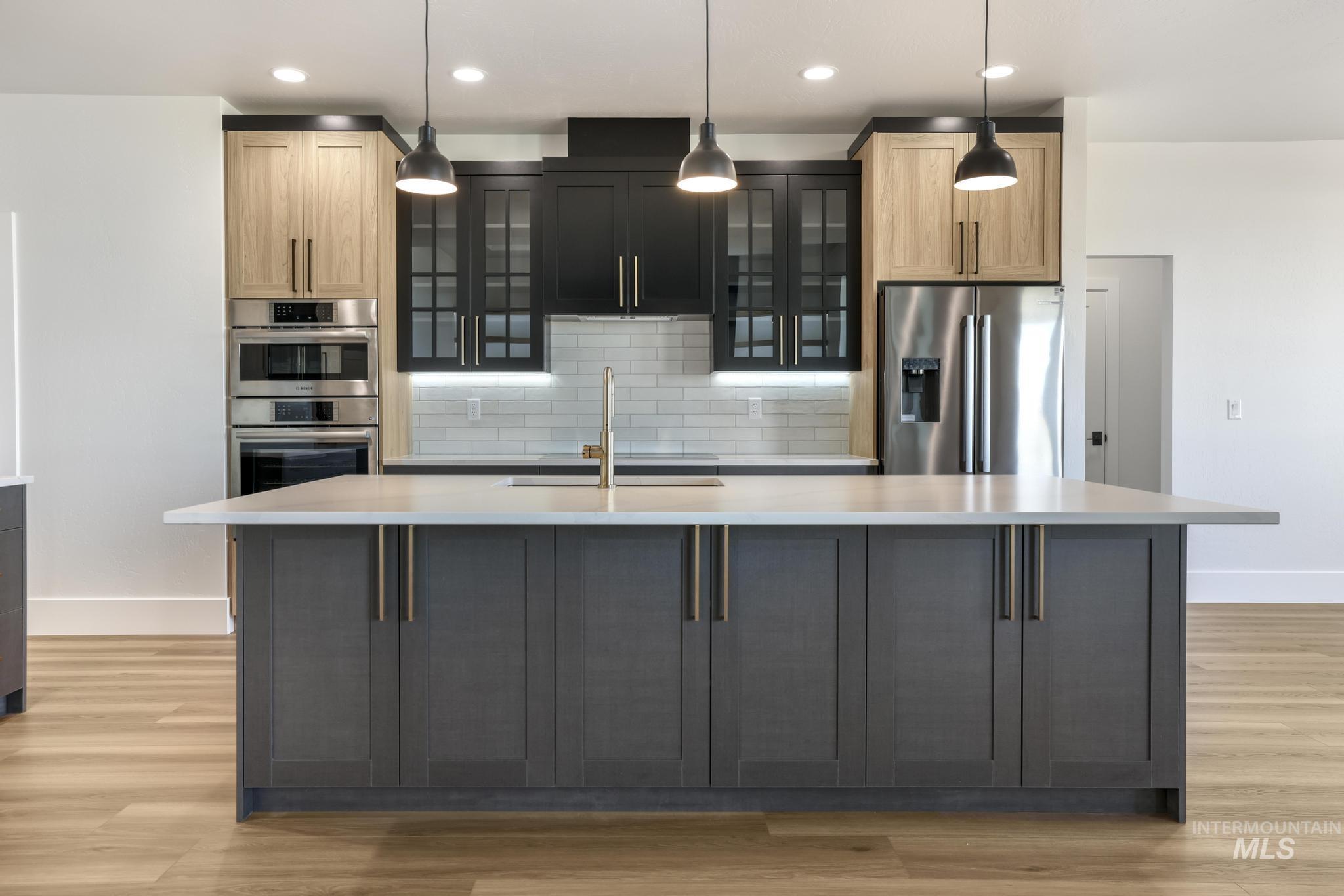 Kitchen featuring stainless steel appliances, decorative light fixtures, glass insert cabinets, light wood-style floors, and recessed lighting