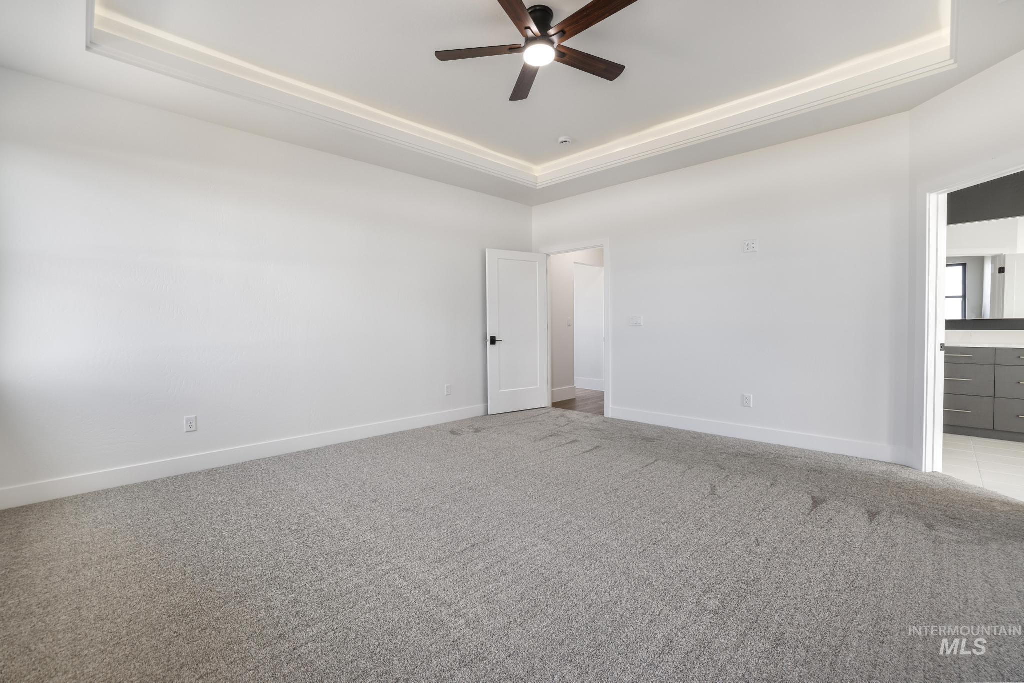 Unfurnished bedroom featuring a tray ceiling, light colored carpet, ceiling fan, and ensuite bathroom