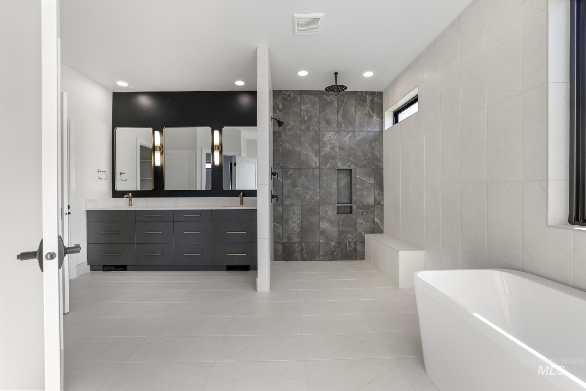 Full bathroom featuring a freestanding bath, double vanity, a walk in shower, light tile patterned flooring, and tile walls