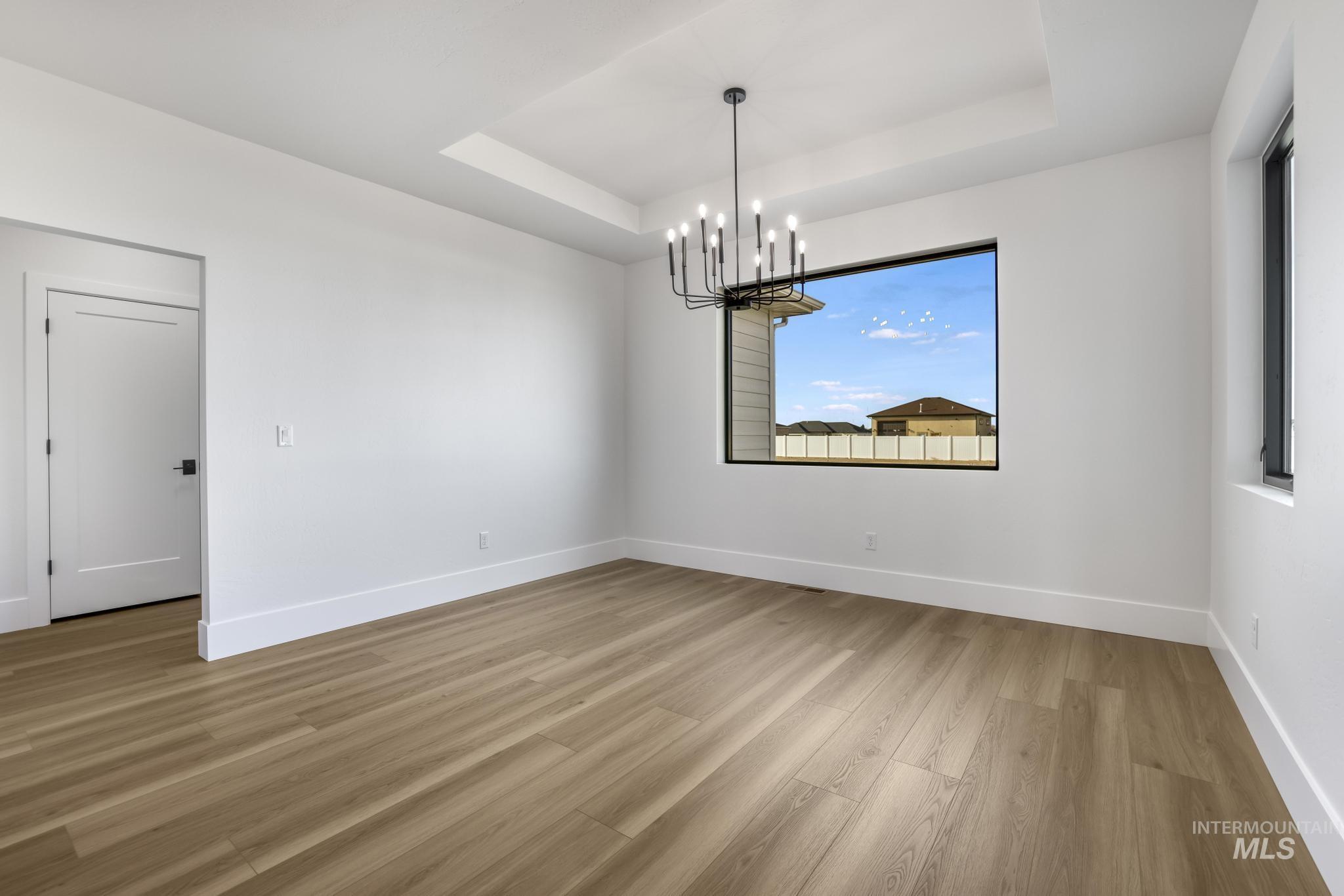 Unfurnished dining area with a raised ceiling, light wood-style floors, and a chandelier