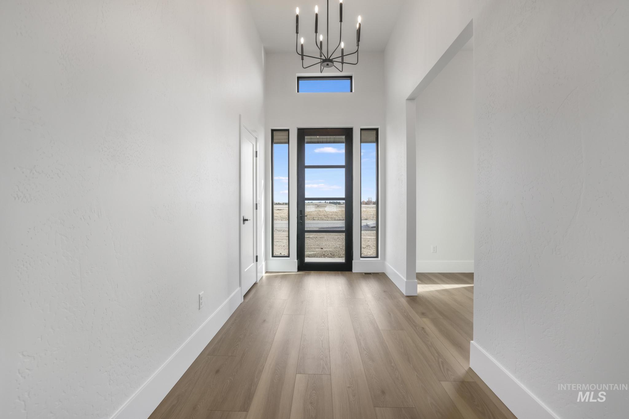 Foyer entrance featuring a chandelier, light wood-style flooring, a high ceiling, and a textured wall