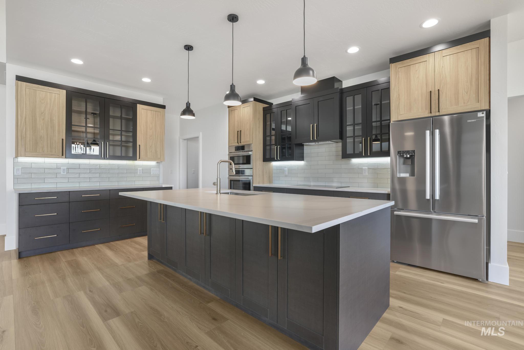 Kitchen with glass insert cabinets, stainless steel fridge with ice dispenser, pendant lighting, an island with sink, and recessed lighting