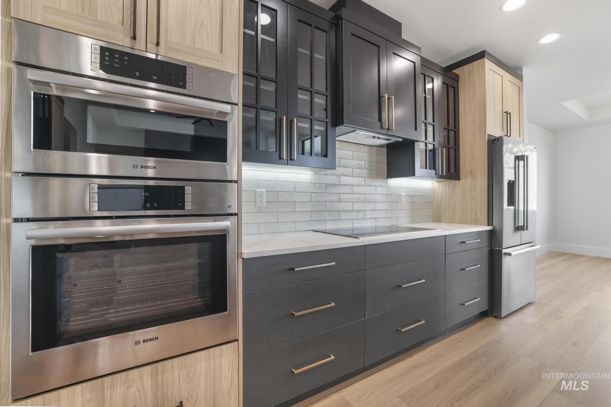 Kitchen with appliances with stainless steel finishes, light wood-style flooring, recessed lighting, glass insert cabinets, and backsplash