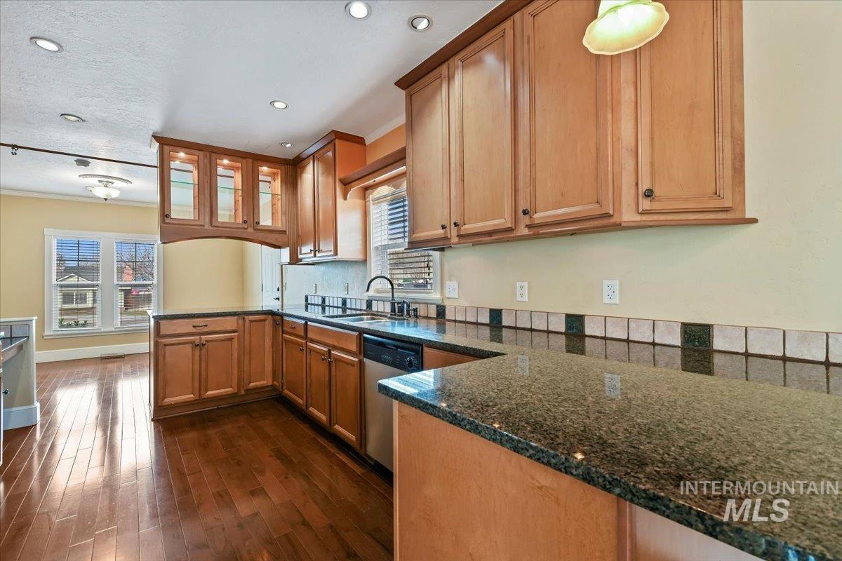 Kitchen featuring a peninsula, ornamental molding, glass insert cabinets, dark stone counters, and dishwasher