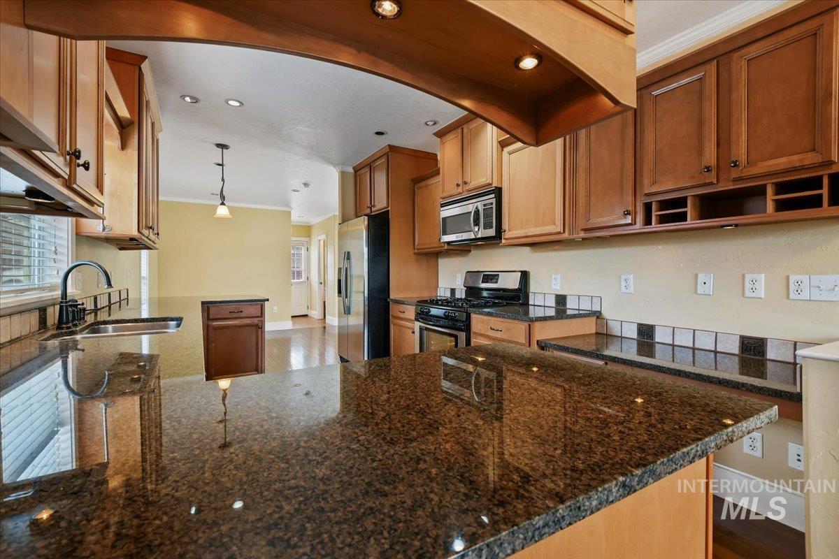 Kitchen with a peninsula, dark stone countertops, stainless steel appliances, ornamental molding, and brown cabinets