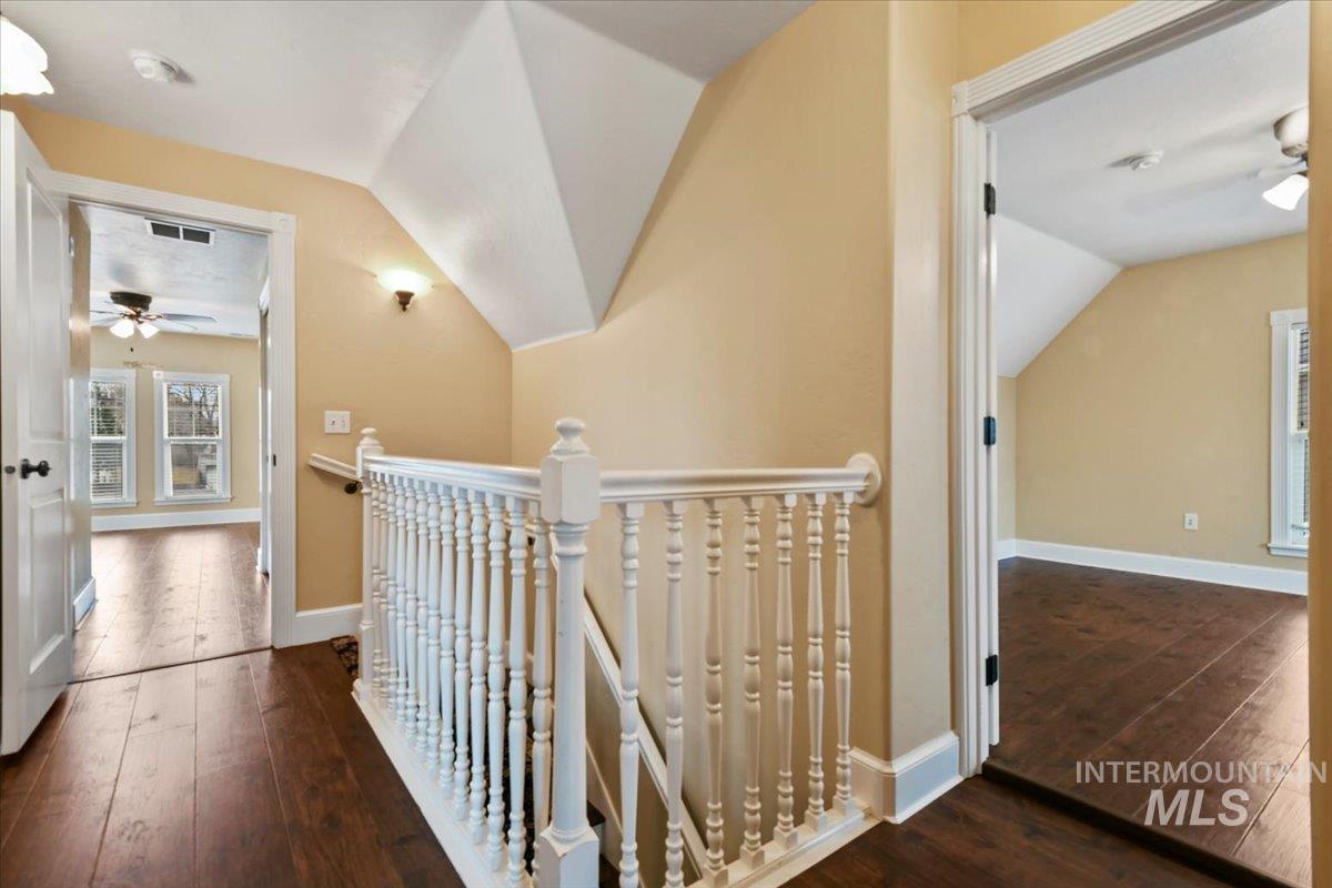 Corridor with an upstairs landing, dark wood-type flooring, and lofted ceiling