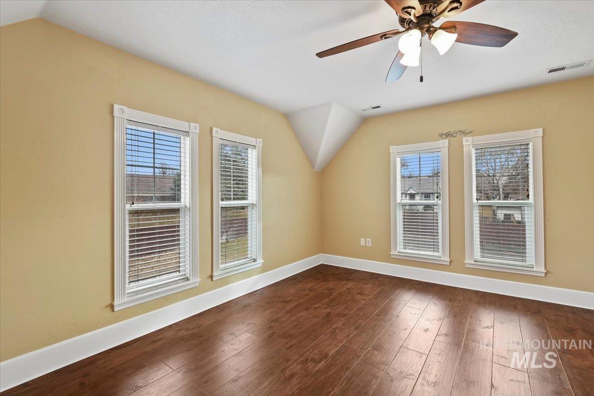 Additional living space featuring plenty of natural light, dark wood-type flooring, vaulted ceiling, and a ceiling fan