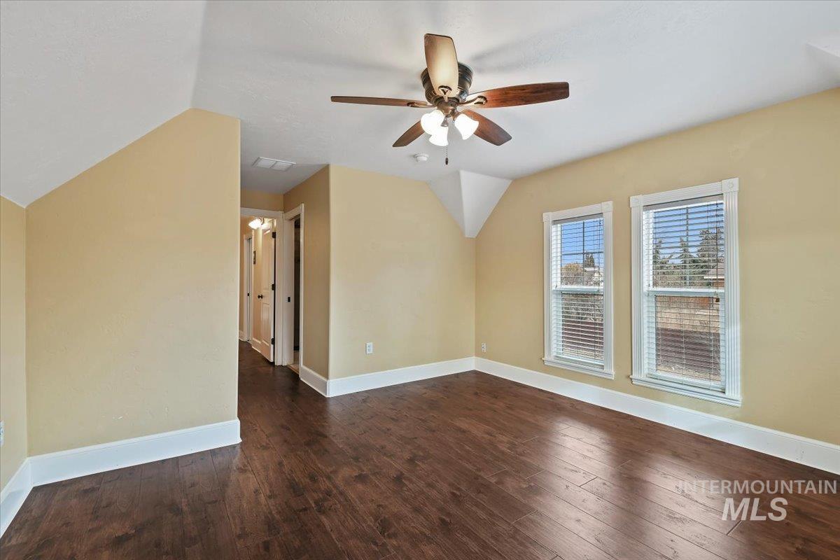 Empty room with lofted ceiling, dark wood-style flooring, and ceiling fan