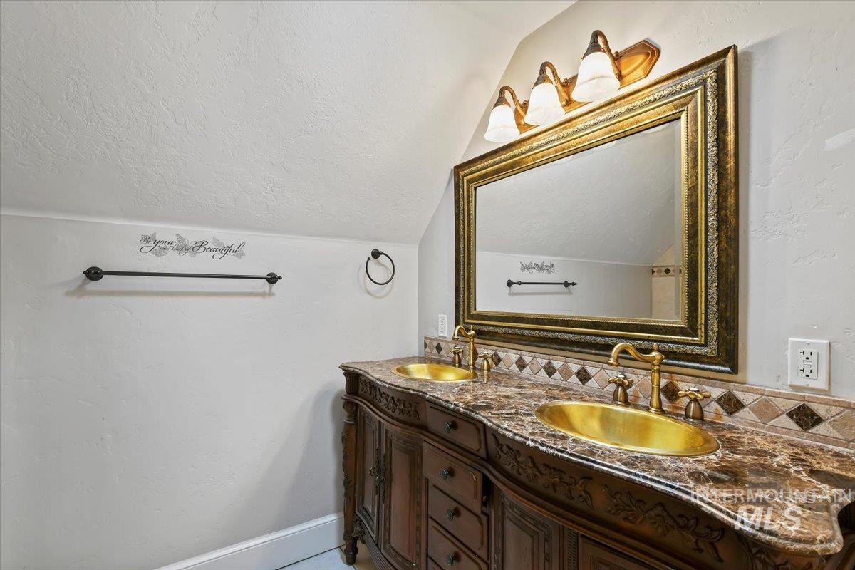 Bathroom with a textured ceiling, double vanity, lofted ceiling, and a textured wall