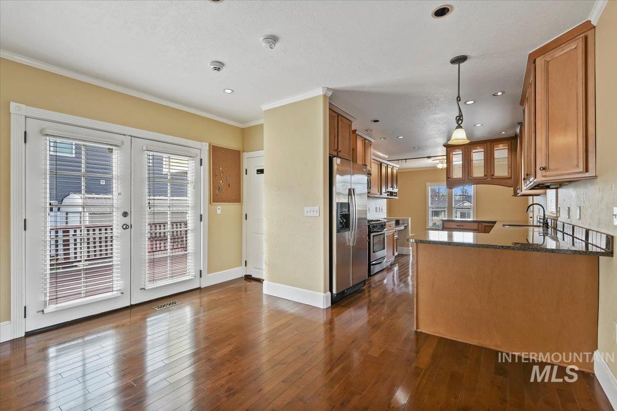 Kitchen featuring dark stone counters, stainless steel appliances, brown cabinets, a peninsula, and hanging light fixtures