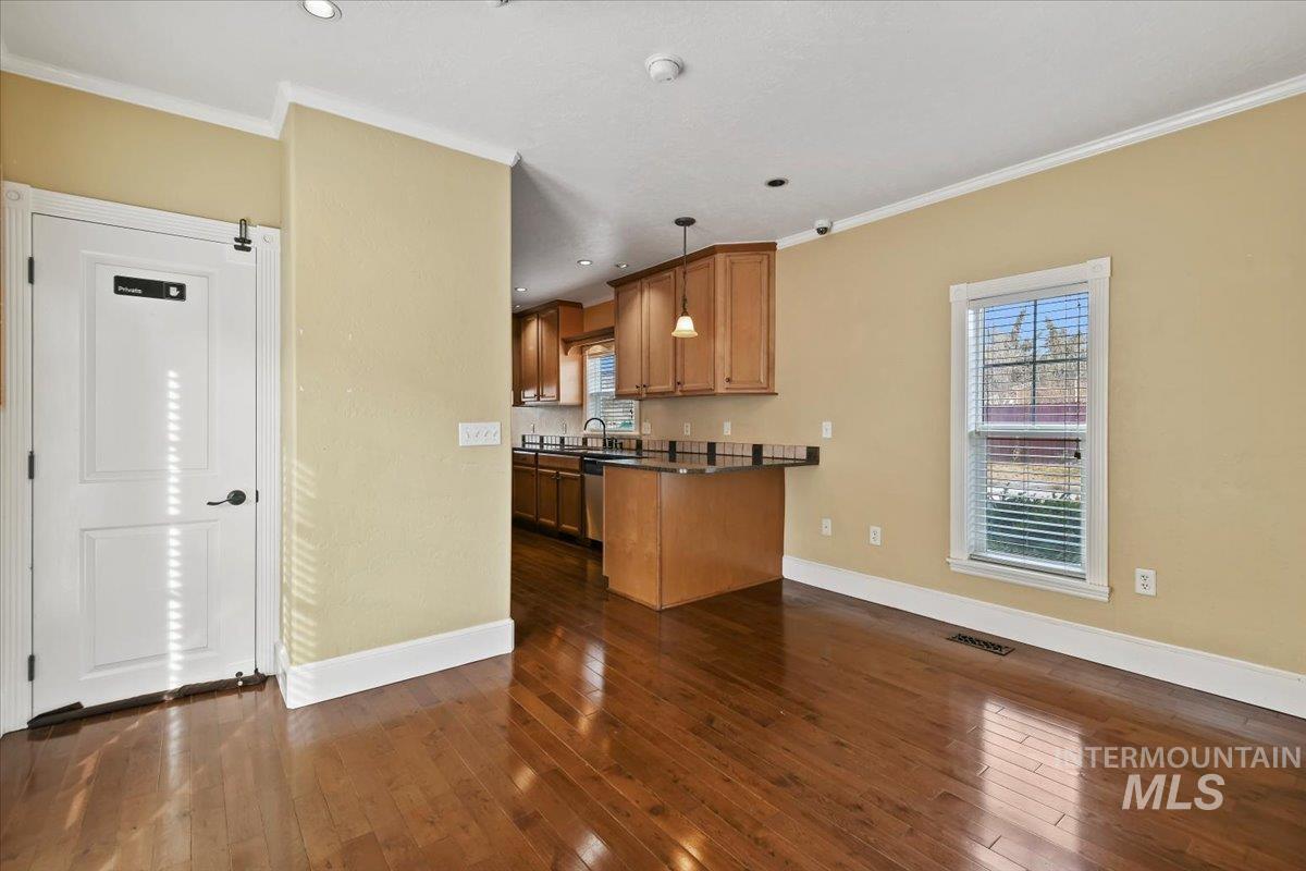 Kitchen featuring decorative light fixtures, ornamental molding, brown cabinets, dark wood-style flooring, and a peninsula