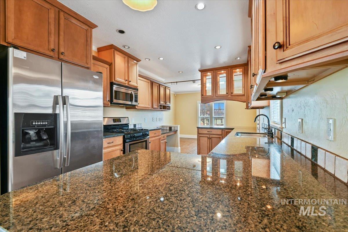 Kitchen with stainless steel appliances, a peninsula, recessed lighting, glass insert cabinets, and dark stone counters