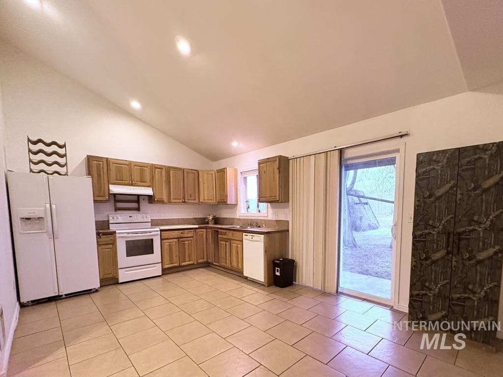 Kitchen with white appliances, under cabinet range hood, high vaulted ceiling, light tile patterned floors, and recessed lighting