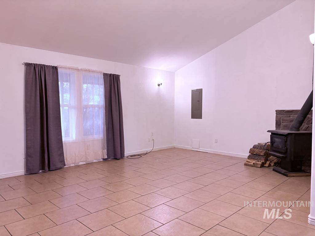 Unfurnished living room featuring a wood stove, lofted ceiling, electric panel, and light tile patterned floors