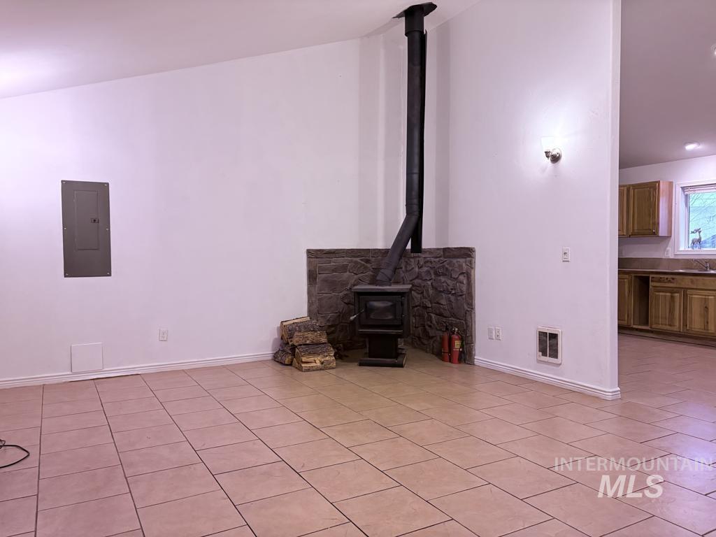 Unfurnished living room featuring a wood stove, electric panel, and light tile patterned flooring